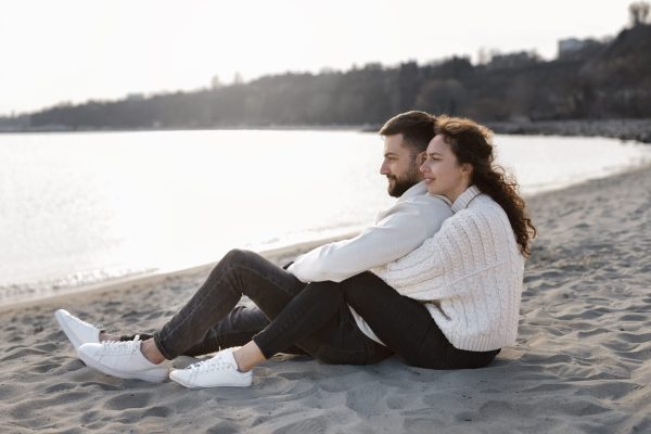 full-shot-happy-couple-sitting-beach-min